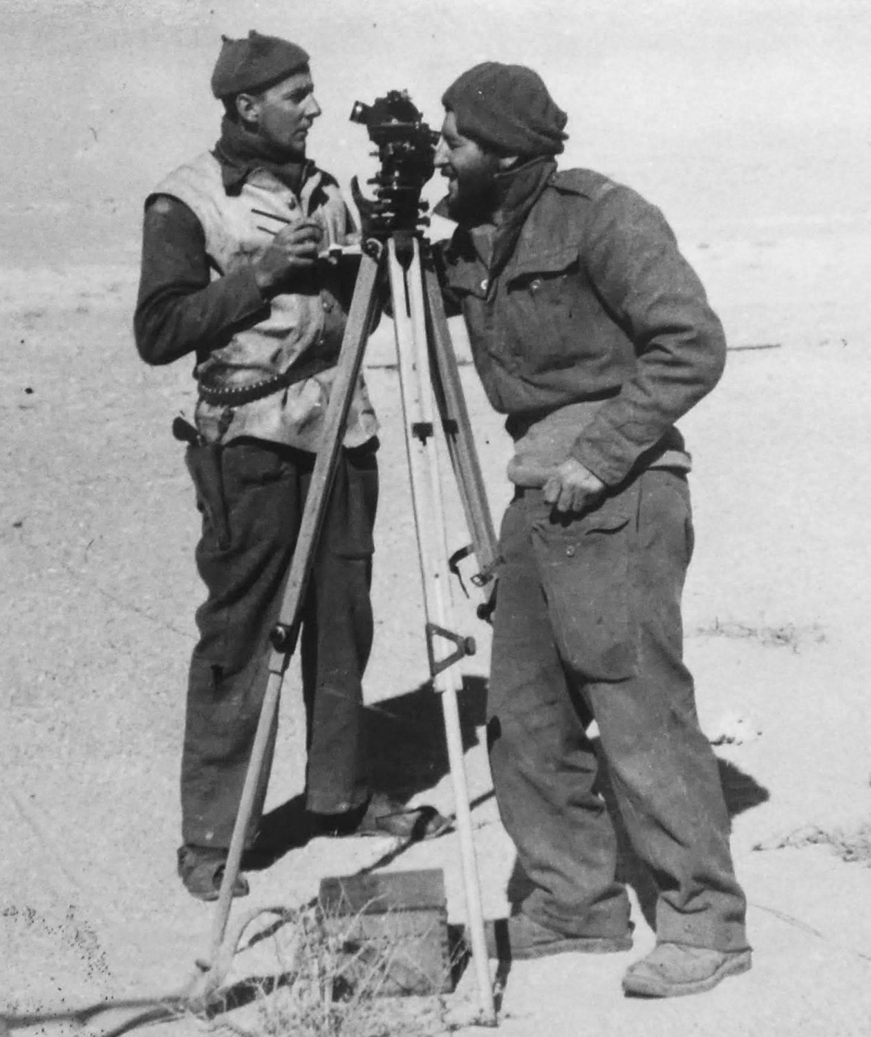 Two LRDG men working a theodolite on a tripod in the desert