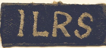 A worn cloth shoulder title, embroidered with the letters I L R S.