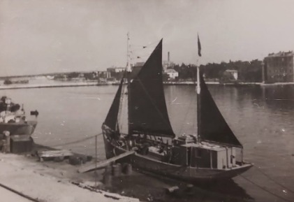 The motor fishing vessel Kufra alongside a quay, her sails set, a town behind